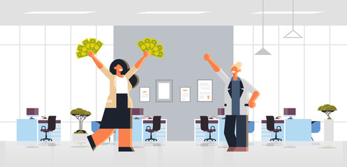 excited businesswoman holding raised dollar cash money rich business women couple standing together financial success concept modern office interior flat full length horizontal
