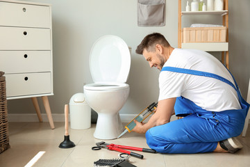Plumber installing toilet in restroom