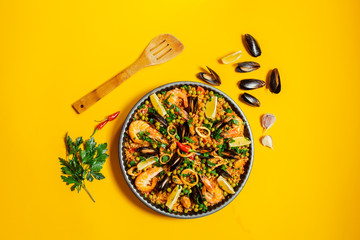 pan with spanish paella with seafood on a yellow background, top view