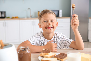 Funny little boy eating tasty toasts with chocolate spreading in kitchen