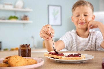 Funny little boy eating tasty toasts with jam in kitchen