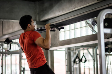 muscular man pulling up bar in gym