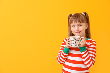 Cute little girl drinking hot chocolate on color background