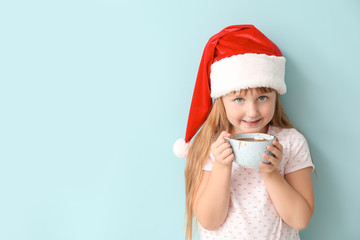 Cute little girl drinking hot chocolate on color background