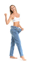 Happy young woman in loose jeans on white background. Weight loss concept