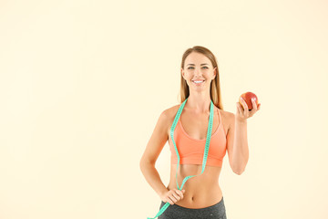 Obraz premium Beautiful sporty woman with measuring tape and apple on color background. Weight loss concept