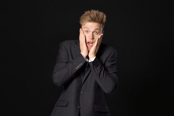 Shocked young businessman on dark background