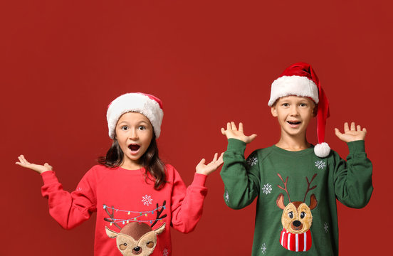 Cute children in Christmas sweaters and Santa hats on color background