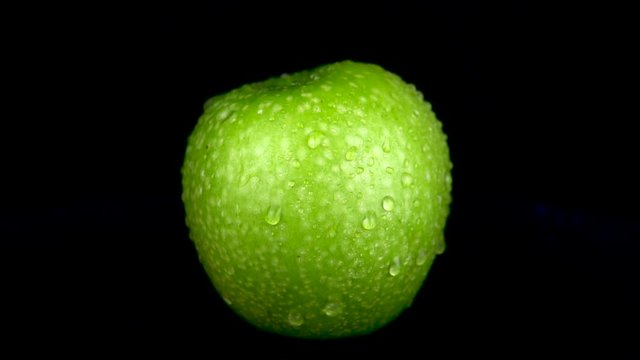 Water is sprayed on a green apple. On a black isolated background. Slow motion