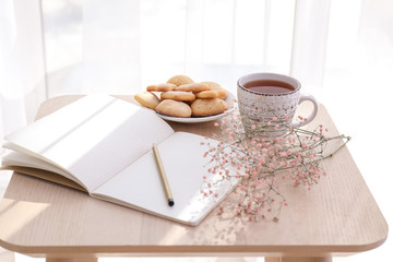 Cup of hot tea with notebook and cookies on table