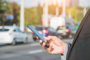 Taxi search or transport, business trip, technology and people concept - close up of young man hand with smartphone on city car road