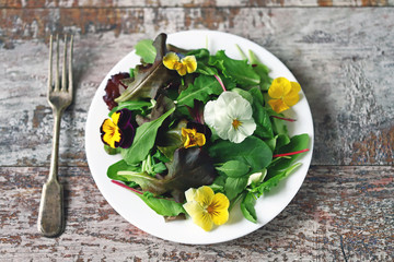 Beautiful mix of salads with flowers on a white plate. Diet concept. Nutrition for girls. Healthy vegan food.