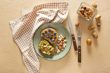 Plate with tasty sweet sandwiches and nuts on color background