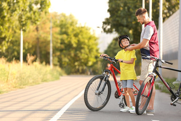 Obraz premium Father helping his son to put on bicycle helmet outdoors