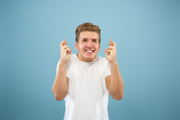 Fototapeta premium Caucasian young man's half-length portrait on blue studio background. Beautiful male model in shirt. Concept of human emotions, facial expression, sales, ad. Showing gesture of good luck.
