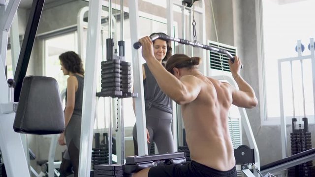 Muscular bodybuilder guy doing Heavy Weight Exercise For Chest talking with woman In The Gym. sport young fitness man training with pull down cable weight machine . couple workout cheer up . friend