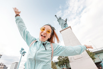 Happy Asian girl traveler funny posing on the background of the famous Statue of Liberty. The...
