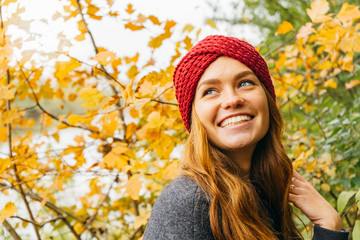 Young happy beautiful girl with red hair in color knitted in an autumn park.