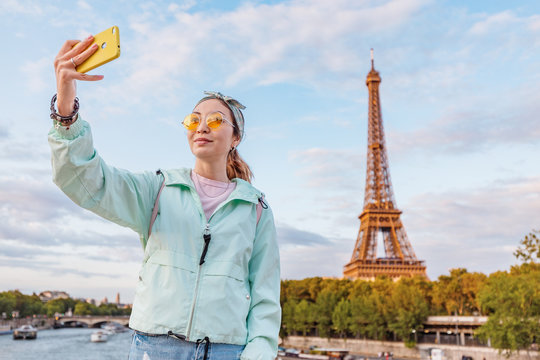 Happy Asian girl traveler makes selfie portrait on mobile phone against Eiffel tower in Paris