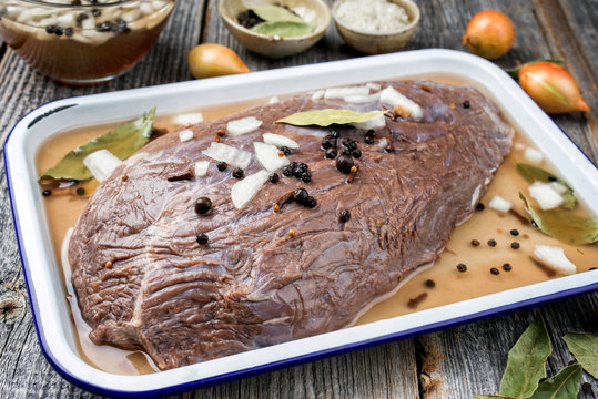 Marinated traditional German Sauerbraten from beef with vegetable and spice as closeup in a white skillet