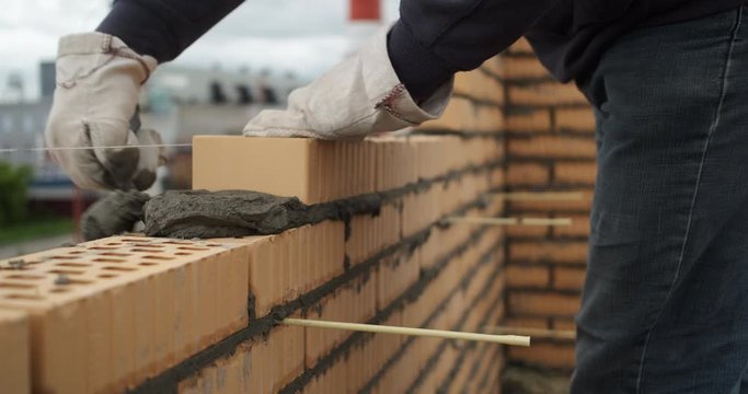 Close-up of builder's hands at work, smoothly put bricks in masonry, builds wall