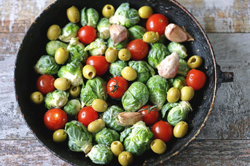 Brussels sprouts in a pan with cherry tomatoes, garlic and olives before baking. Healthy food. Vegan diet. Vegetable pan.