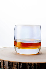 Glass of whiskey on a wooden board. Wooden saw cut. White background. Whiskey / Brandy / Cognac / Rum. Glass with a strong drink.