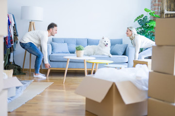 Young beautiful couple with animal moving sofa at new home around cardboard boxes