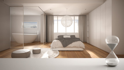 White table or shelf with crystal hourglass measuring the passing time over minimalist bedroom with bathroom and window, architecture interior design, copy space background