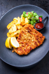 Deep fried Wiener schnitzel from veal topside with French fries and lettuce as closeup on a modern...