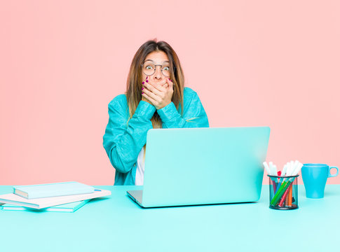 young pretty woman working with a laptop covering mouth with hands with a shocked, surprised expression, keeping a secret or saying oops