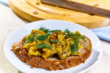 Sandwich with relish with cucumbers lies on a white plate on the background of bread