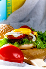 Burger with cutlet, tomatoes and egg is on a wooden Board