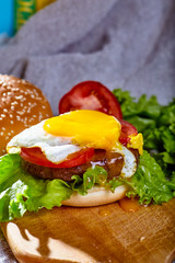 Burger with cutlet, tomatoes and egg is on a wooden Board