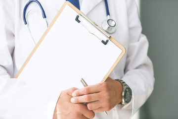 Close-up of clipboard with blank paper in medical doctor hand. Male doctor listens to the patient...