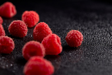 Chaotically scattered ripe raspberries on a black surface with water droplets. Close up.