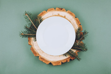 Festive Christmas natural style table setting with white plate on wood cut platters and fir tree...