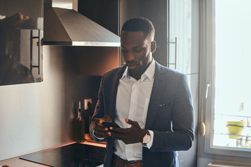 Young african man in white shirt is chatting by mobile phone at the kitchen.