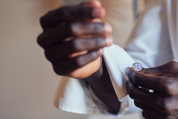 Closeup photo shoot of african american man in white shirt with diamond cufflink in hand.