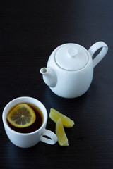 Tea with lemon in a white cup and a white teapot on a dark background