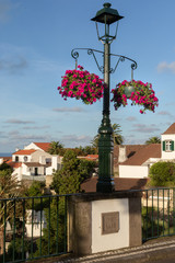 Fototapeta na wymiar Lamp post on a bridge adorned by blooming flowes in Nordeste town, Sao Miguel island, Azores