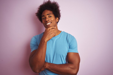 Fototapeta na wymiar African american man with afro hair wearing blue t-shirt standing over isolated pink background looking confident at the camera with smile with crossed arms and hand raised on chin. Thinking positive.