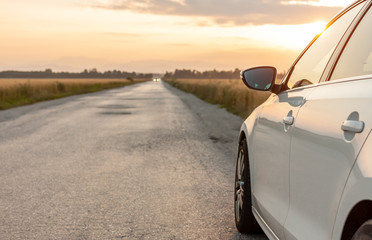 white car on country road next to yellow wheat field