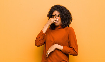 young pretty black woman feeling disgusted, holding nose to avoid smelling a foul and unpleasant...