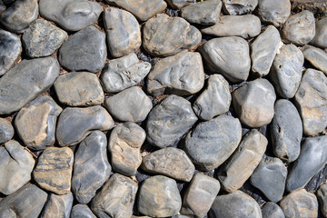 Grungy photo texture of grey stone. Round rocks top view background. Seaside stone paving under sunlight.