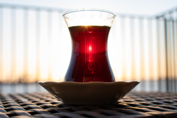 Turkish Cay Tea (çay is translated tee) in traditional clear glass with sunset behind the glass in Izmir. Black tea in clear glass.