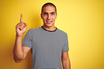 Fototapeta premium Young handsome man wearing striped t-shirt over yellow isolated background pointing finger up with successful idea. Exited and happy. Number one.
