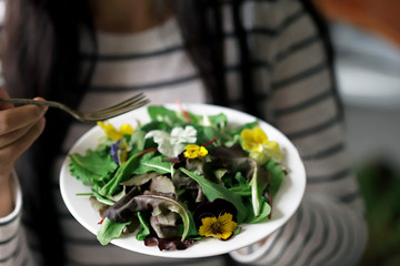 Selective focus. A beautiful mix of salads with flowers on a white plate is held by a girl. Diet concept. Healthy vegan food.