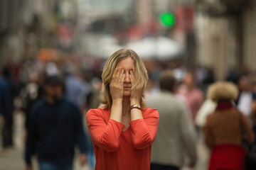 Panic attack in public place. Young woman covers his eyes with hands at standing in the middle of a busy street.