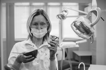 Portrait of female dentist with tools over medical office background. Black and white photo..